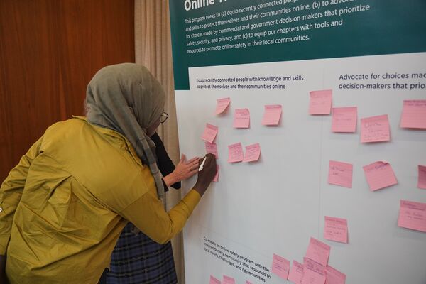 A woman in a hijab writes on a poster covered in colorful sticky notes
